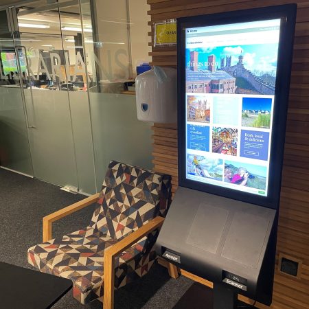 The NHS Digital Community Kiosk standing in the University of Lincoln Library next to an armchair.